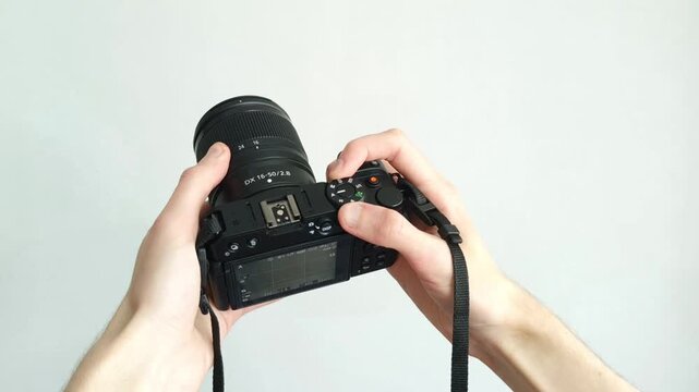 Professional photographer hand holds modern black camera with lens against clean background.