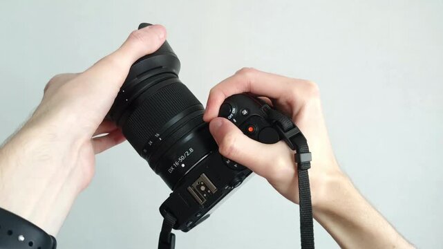 Human hand firmly holds professional camera with lens hood pointing forward on white background