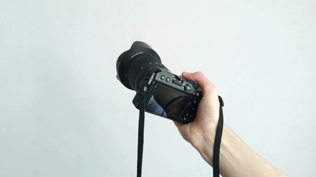 Human hand firmly holds professional camera with lens hood pointing forward on white background