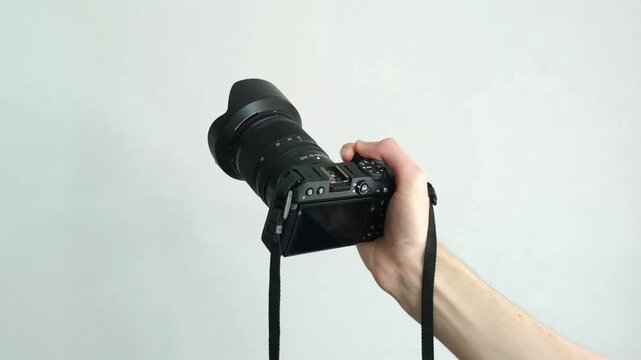Human hand firmly holds professional camera with lens hood pointing forward on white background