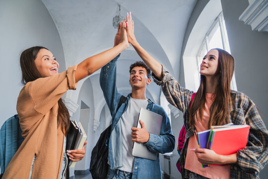 Group of high school students giving high five in school corridor, classmates celebrating teamwork, friendship, success, education, learning and student life concept