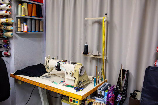 Industrial sewing machine in a professional tailoring workshop with thread stand and sewing supplies. Textile equipment used for garment production, clothing repair, stitching and fabric manufacturing