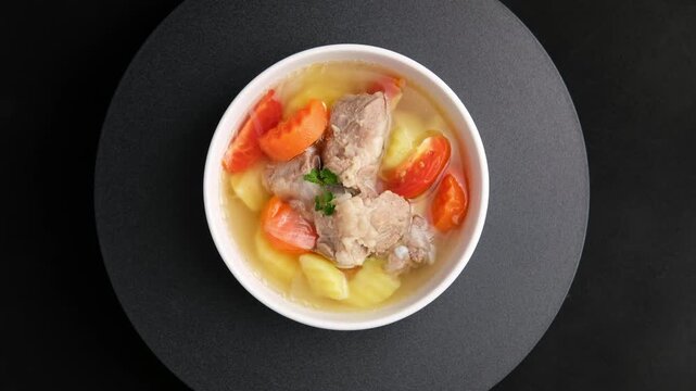 Clear Pork Soup with Soft Bone (Pork Cartilage Soup).Potatoes Soup With baby pork rib carrot tomato and onion in white bowl.Top view.