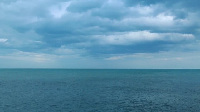 Dramatic dark storm clouds moving over the vast turquoise sea. Moody ocean landscape, coastal weather changes, and natural tropical seascape environment under overcast sky.