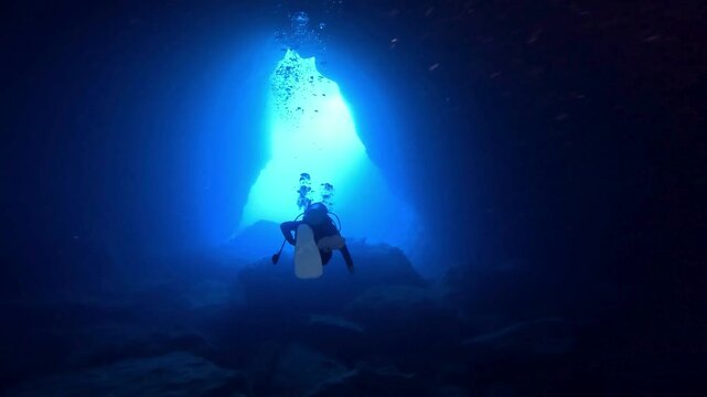 Scuba diver swimming towards a light opening in an underwater sea cave, 4k video