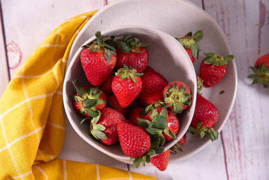 Fragole fresche dentro ciotola bianca su tavola con tovaglia bianca, visti dall'alto