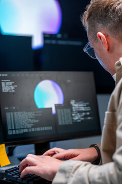 A concentrated young Caucasian IT specialist indicates a line of code on the monitor at a glowing command-centre workstation at night, securing enterprise systems.
