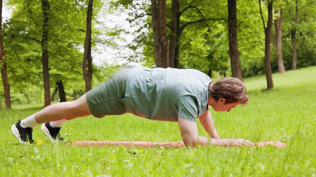 A healthy man doing a dynamic plank exercise on a fitness mat during an outdoor workout and training session in a green park. High quality 4k footage