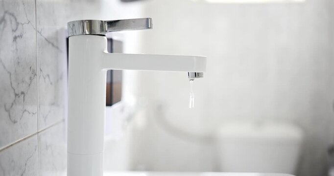 Thin stream of water leaking and dripping from the calcified aerator of a modern white bathroom faucet in a low angle shot in real time.