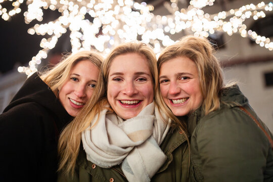 Three young women friends smiling outdoor under bright lights