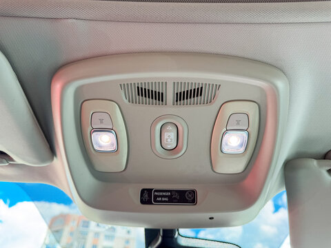 View of car interior lights and controls located on the ceiling, showing features during daylight in a parked vehicle in an urban area