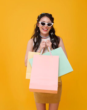 Asian woman holding colorful shopping bags and wearing sunglasses celebrating retail joy consumer confidence seasonal sales youthful fashion and vibrant modern lifestyle.