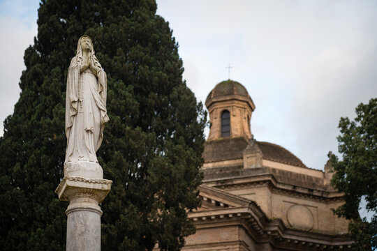 Close up of the marble statue of Virgin Mary with the blurred dome of Santa Maria Scala Coeli church in the background at Tre Fontane Abbey in Rome, Italy