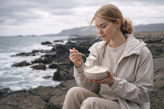 Woman eating skyr on a rocky Icelandic coast, capturing serene moments