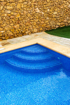 Blue Mosaic Pool Steps Against Rustic Stone Wall With Patio and Lawn, Outdoor Relaxation