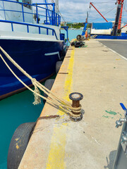 Fototapeta premium Boat is tied at the dock near the harbor with a rope attached to a pulley and a clear view of the turquoise water in the background