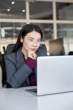 Dark-haired asian young manager sitting at the laptop and looking involved