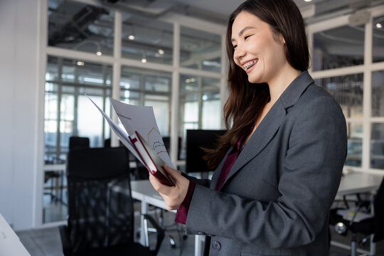 Smiling young woman holding documents in hands and looking contented