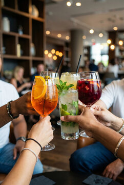 Beautiful raster photograph capturing a diverse group of people toasting with fresh colorful summer cocktail drinks celebrating in a warm blurred restaurant bar bokeh setting