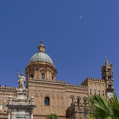Fototapeta premium Santa Rosalia statue in front of Palermo Cathedral in Sicily, Italy. Beautiful view of the historic church dome, Norman bell tower, and a palm tree under a blue sky.
