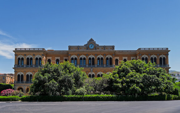 Facade of Stazione di Palermo Centrale railway station at Piazza Giulio Cesare square in Sicily, Italy. Historic grand building with central clock tower framed by green trees.