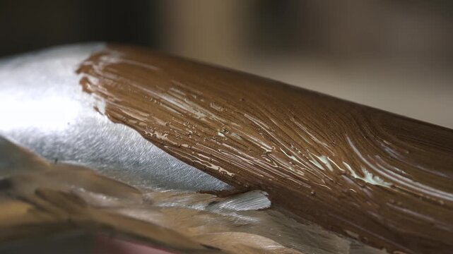 A decorator paints a metal broomstick pipe, using a special paint to create a wood grain effect.
