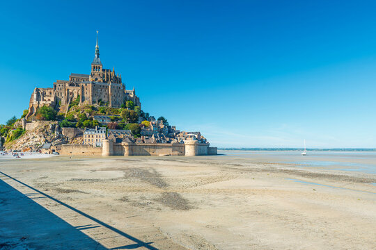 Mont Saint Michel abbey at low tide under clear blue sky with medieval architecture and coastal landscape in Normandy, France. Tidal island with gothic cathedral in Normandie. French countryside