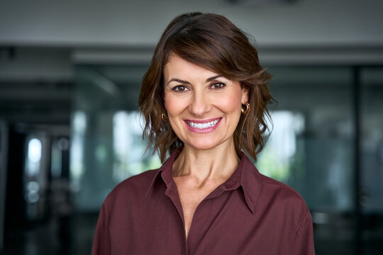 Close up portrait of happy latin businesswoman looking at camera in office. Smiling mature woman shows beautiful face with toothy smile. Cheerful female business executive enjoys career at work.