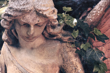 Fototapeta premium Ancient cemetery angel statue surrounded by ivy. Symbol of remembrance, faith, hope, eternal peace and divine protection.