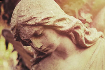 Fototapeta premium Ancient cemetery angel statue bathed in warm sunlight. Symbol of remembrance, faith, hope, eternal peace and divine protection.