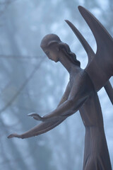 Fototapeta premium Ancient angel statue standing in the rain with outstretched hands. A symbol of protection, hope, faith and compassion through life's darkest moments.