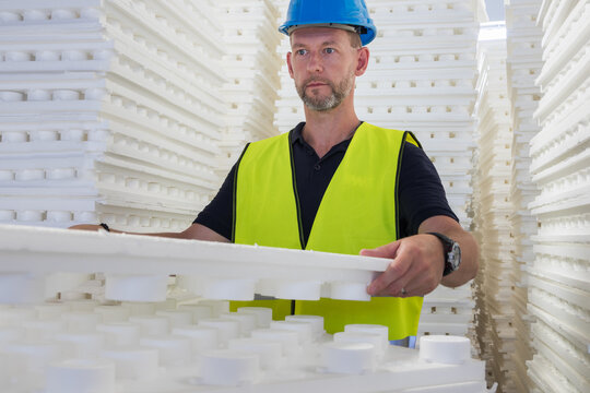 Construction worker in a blue hard hat and safety vest working with white polystyrene insulation sheets