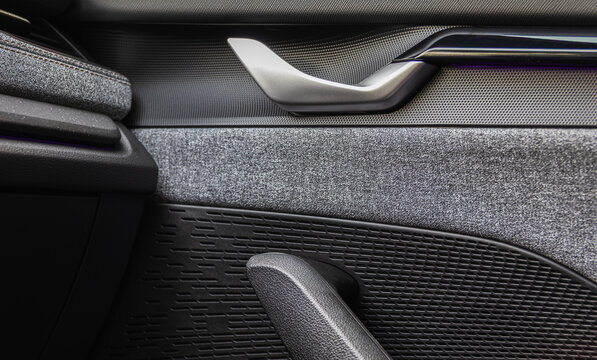 Close-up of a modern car door panel interior with a metallic handle, fabric upholstery, and speaker grille