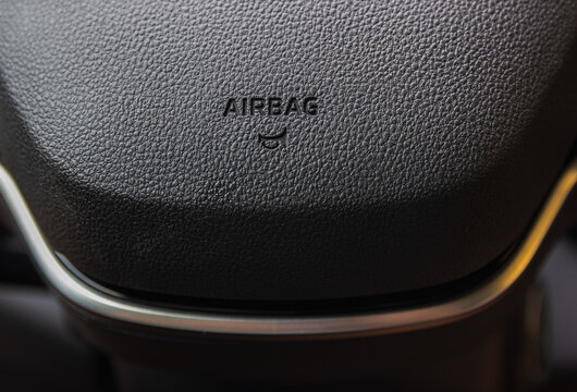 Close-up of a car steering wheel with the airbag text and horn icon on a black leather texture