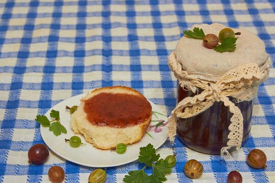 Homemade gooseberry jam in a glass jar with fresh berries, Gooseberry jam jar and bread with jam on checkered tableclot