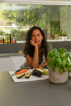 Thoughtful Hispanic woman in modern kitchen surrounded by fresh ingredients