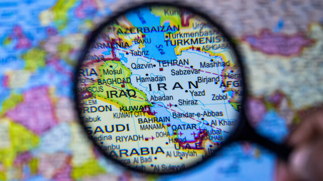 magnifying glass highlighting iran and surrounding middle eastern countries on a colorful world map.