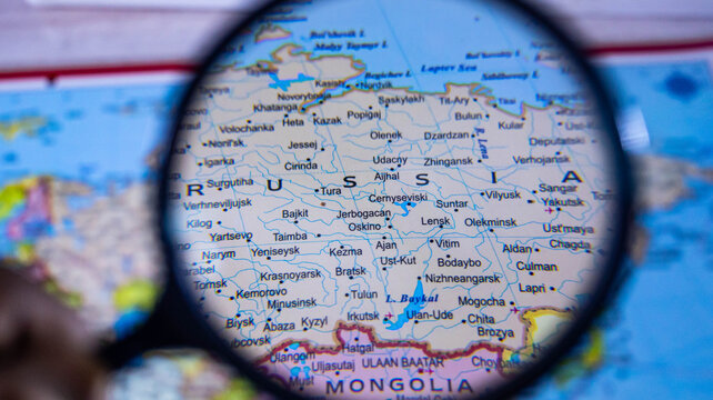 Magnifying glass on world map focusing on central russia and surrounding cities.