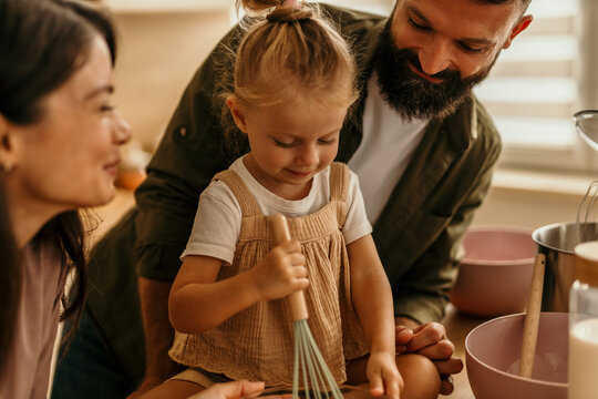 Family baking together in kitchen, child whisking ingredients