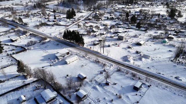 mooth cinematic drone footage flying backward over a quiet snow-covered rural residential area in Northern Europe. The aerial view reveals detached homes, country roads, gardens and winter scenery