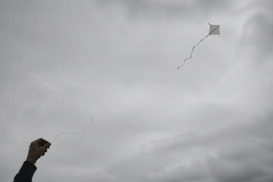 Broken kite string, kite drifting away in gray overcast sky, minimalist composition.