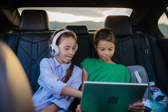 Little sisters sitting in car, playing on tablet and smartphone.