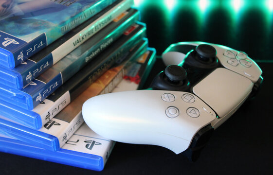 PlayStation 5 DualSense controller beside PS4 and PS5 game cases under green LED lighting. Modern gaming setup featuring console technology and physical game collection.