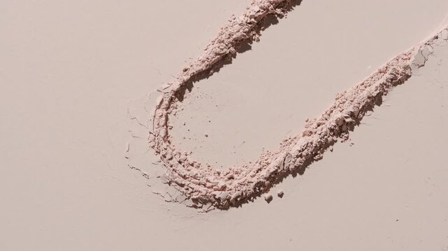 Top perspective capture of a beige smoothened powder surface with a dragged circle imprint illuminated by moving light, casting fluid and shifting shadows | Promotional concept for matte powder