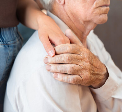 A young woman's hand holds the hand of a senior adult man, comforting or sympathizing with him. Concept of Caregiver Support and Home Care