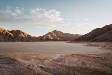 Golden hour view of a dramatic desert basin surrounded by rugged mountains beneath a soft blue sky with scattered clouds, showcasing an arid natural landscape and peaceful wilderness scenery. © AI illustration 