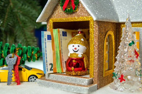 Near the house with a snowman and euro bills on the porch there is a yellow car with keys