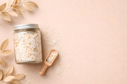 Glass Jar with Sea Salt Wooden Scoop and Dried Leaves on Beige Background