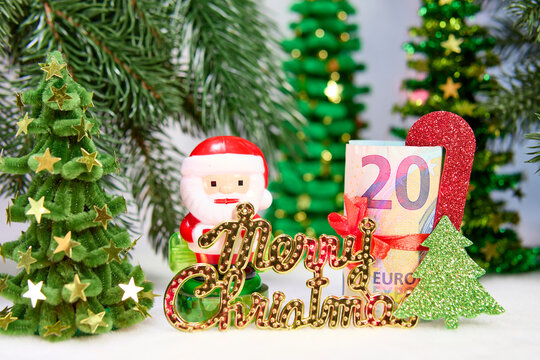 Santa Claus with letters and a euro banknote with decorations against a background of Christmas trees
