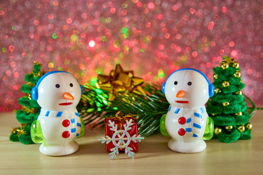 Unusual snowmen and a snowflake with a gift near a Christmas tree branch and fir trees on a colored background